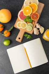 food, healthy eating and vegetarian concept - close up of citrus fruits, wooden cutting board and notebook on slate table top