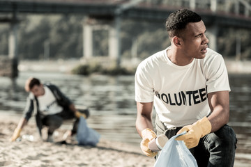 Socially active. Handsome dark-haired student wearing white shirt being socially active while cleaning the beach