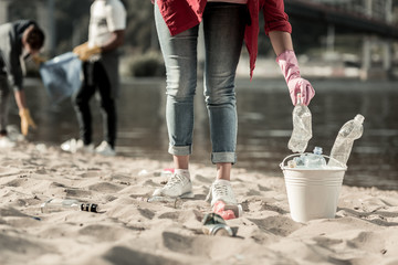 Trash on beach. Active responsible student wearing jeans volunteering while cleaning up trash left...