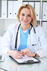 Doctor woman at work. Portrait of cheerful smiling blonde physician sitting at the desk. Medicine and healthcare concept