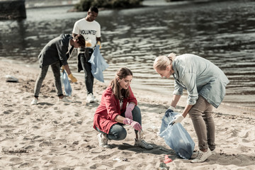 Helpful teacher. Caring blonde-haired teacher wearing denim shirt helping her students volunteering at the beach