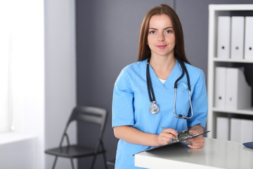 Doctor woman at work. Portrait of female physician filling up medical form while standing near reception desk at clinic or emergency hospital. Medicine and healthcare concept