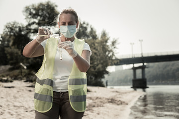 Pouring water. Experienced sanitary inspector wearing mask and yellow vest pouring river water into...