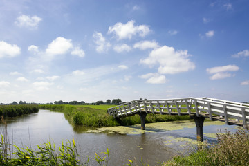 Typical Dutch landscape with green meadows, grass, bridge, water, blue sky and clouds