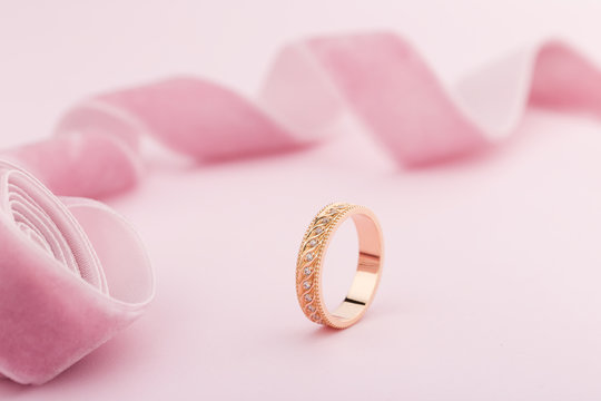 Pink Gold Wedding Ring With Diamonds And Wave Pattern On Pink Background