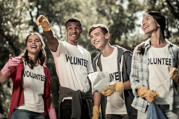 Volunteer sign. Beaming funny students wearing white shirt with volunteer sign feeling responsible while cleaning forest