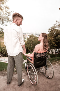 No barriers. Beautiful couple looking happy and kind cheerful man holding hand of his disabled girlfriend
