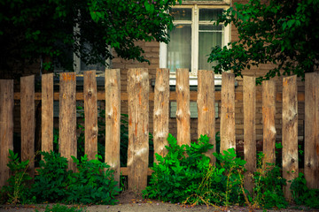 Naklejka premium Old wooden fence with grass in the foreground and brick house in the background