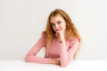 Obraz na płótnie Canvas Studio portrait of a beautiful girl blonde teenager on a white background sitting at the table.
