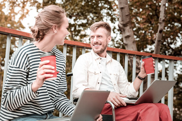 Working day. Relaxed young people enjoying coffee in the park and talking while holding modern...