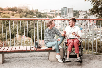 Involved in talk. Young disabled man sitting in the park near his young friend and enjoying...