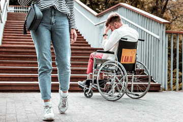 No attention. Young woman walking and paying no attention to the sad disabled man sitting in the...