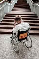 Alone with difficulties. Unhappy depressed disabled man sitting in the wheelchair in front of...