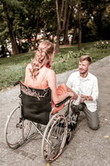 Obraz premium Unusual couple. Handsome serious man gently looking at his disabled girlfriend while sitting in front of her