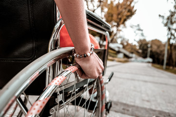 Naklejka premium Hand on wheel. Close up of young girl sitting in the wheelchair and putting her hand on the wheel