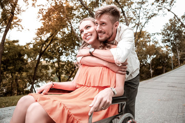 Hugging invalid girlfriend. Romantic young man gently hugging his disabled girlfriend while...
