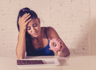 Pretty latin woman looking at chocolate and donuts tired of diet restrictions