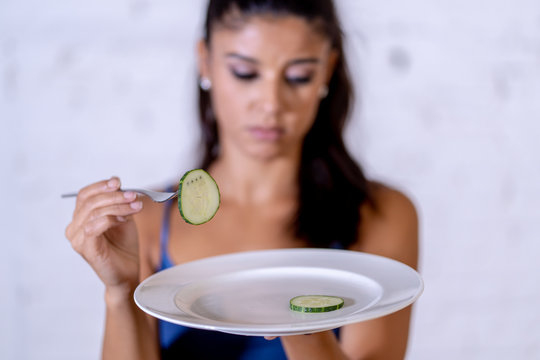 Depressed dieting woman holding folk looking at small green vegetable on empty plate