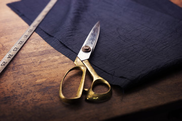 Measuring and cutting textile or fine cloth. Work table of a tailor. Gold scissors and black silky...