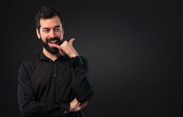 Handsome man with beard making phone gesture on black background