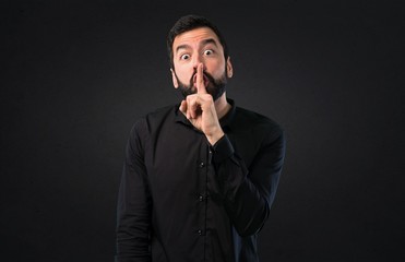 Handsome man with beard making silence gesture on black background