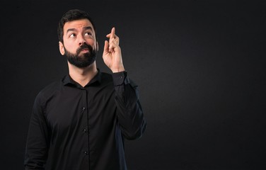 Handsome man with beard with his fingers crossing on black background