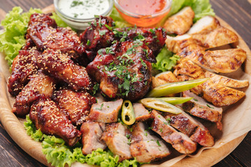 Big plate with grilled meat and sauces on dark wooden table