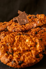 Chocolate chip cookies on rustic dark black background. Stacked chocolate chip cookies on brown napkin. Freshly baked. Concept for a tasty snack. Sweet dessert. Selective focus. Close up.