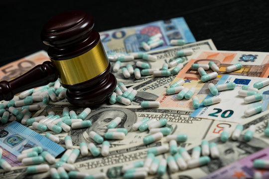 Wood judge's gavel and scattered colorful drugs on the dollar and euro cash background