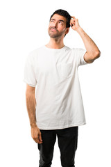 Fototapeta premium Young man with white shirt having doubts and with confuse face expression while scratching head on isolated white background