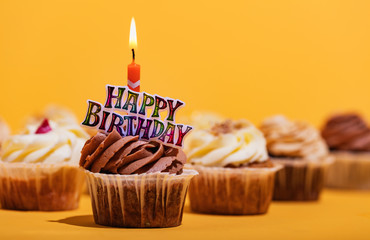 Birthday muffin with candle on yellow background.