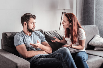 Family arguments. Sad unhappy depressed woman looking at her husband and shouting at him while arguing