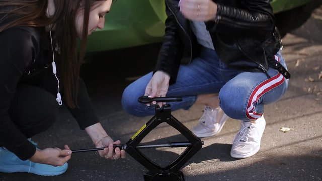 Two women know how to operate the Jack to change a punctured wheel of the car.