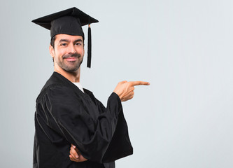 Man on his graduation day University pointing finger to the side and presenting a product in...