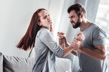 Humans rights. Angry depressed strong man looking at his wife and using his strength while holding her hands