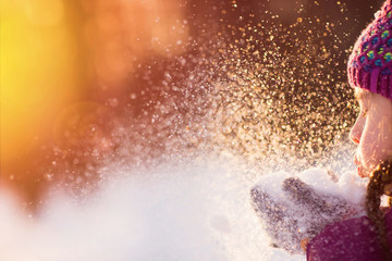 Baby girl blowing snow in frosty winter park. Flying Snowflakes. Sunny day. Backlit. Child to have...