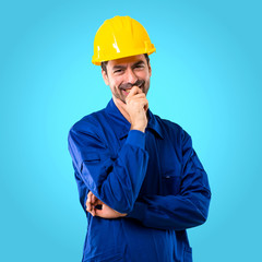 Young workman with helmet smiling with a sweet expression on blue background