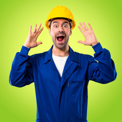 Young workman with helmet with surprise and shocked facial expression. Gaping because can not believe what is happening on green background