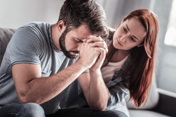 Difficult times. Sad depressed cheerless man sitting on the sofa and thinking about his problems while holding his forehead