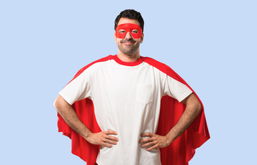Superhero man with mask and red cape posing with arms at hip and laughing looking to the front on...