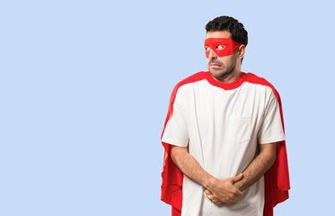 Superhero man with mask and red cape is a little bit nervous and scared pressing the teeth on isolated blue background © luismolinero