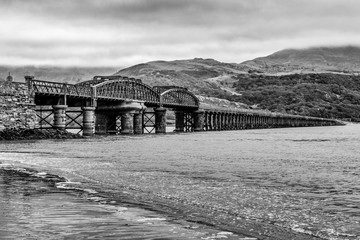 Black and White Railway bridge at Barmouth over River Mawddach, Wales UK on cloudy day with moody skies