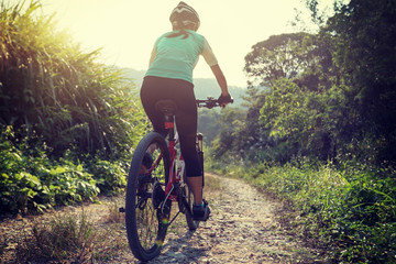 Naklejka premium Woman cyclist riding mountain bike on rocky trail at sunny day