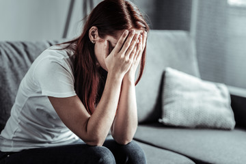 Want to hide. Negative delighted female leaning elbows on knees, bowing head while covering her face