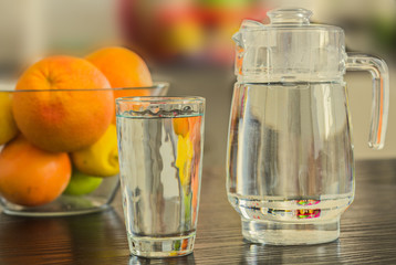 Pitcher and glass of water with bowl of fruits on the background.