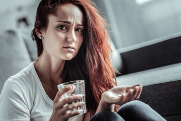 Do not like it. Negative delighted girl wrinkling forehead while suffering headache, taking medicine