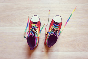 Sneakers LGBT colors. Fashionable shoes  with untied shoelaces on wooden background. top view.    - obrazy, fototapety, plakaty