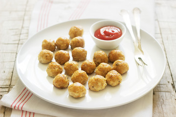 Homemade little chicken meatballs with tomato sauce on a wooden table.