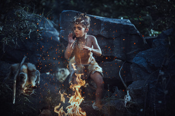 Shaman boy at the fire. Scary young primitive boy outdoors near bonfire. Witch craft concept. Angry...