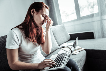 Try to work. Serious young woman bowing head while holding laptop on knees and trying to concentrate